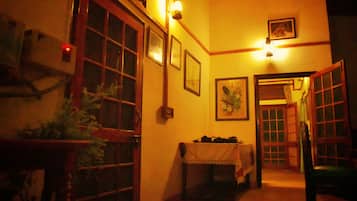 A dimly lit corridor with wooden doors and windows, a table with a white tablecloth, and framed pictures on the walls.