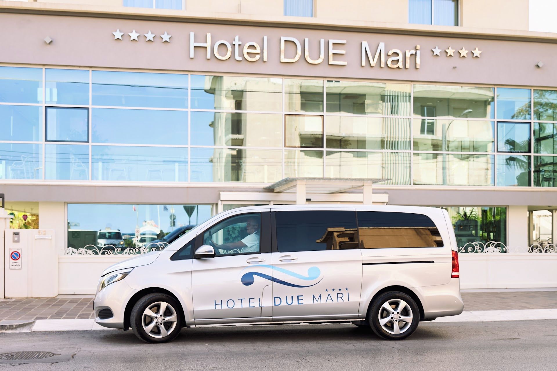 A white van parked in front of Hotel DUE Mari with a clear view of the building's facade.