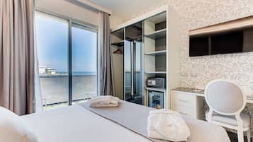 Habitación de hotel con cama, escritorio, silla, minibar y un ventanal con cortinas.