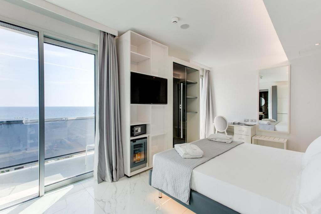 Una habitación de hotel moderna con una cama grande, un televisor de pantalla plana, un vestidor y un balcón con vistas a la ciudad.