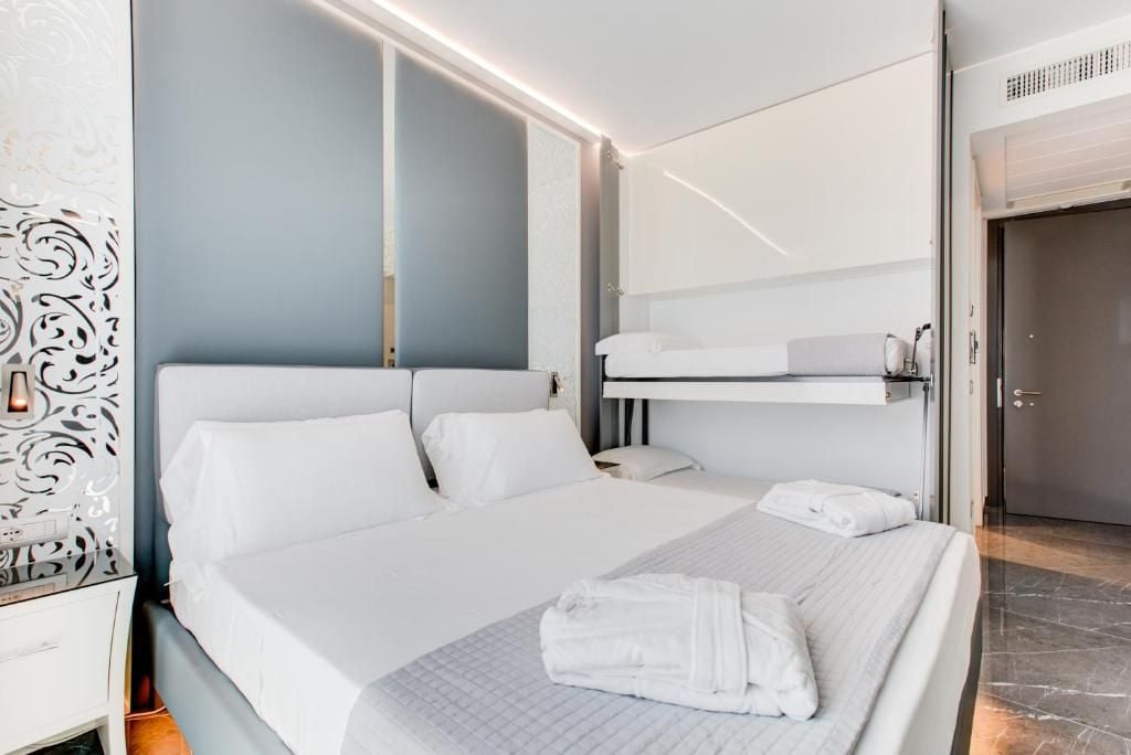 Ein modernes Hotelzimmer mit einem großen Bett, einem Nachttisch, einem Kleiderschrank und einer eingebauten Sitzbank über dem Bett.