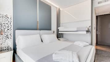 Ein modernes Hotelzimmer mit einem großen Bett, einem Nachttisch, einem Kleiderschrank und einer eingebauten Sitzbank über dem Bett.