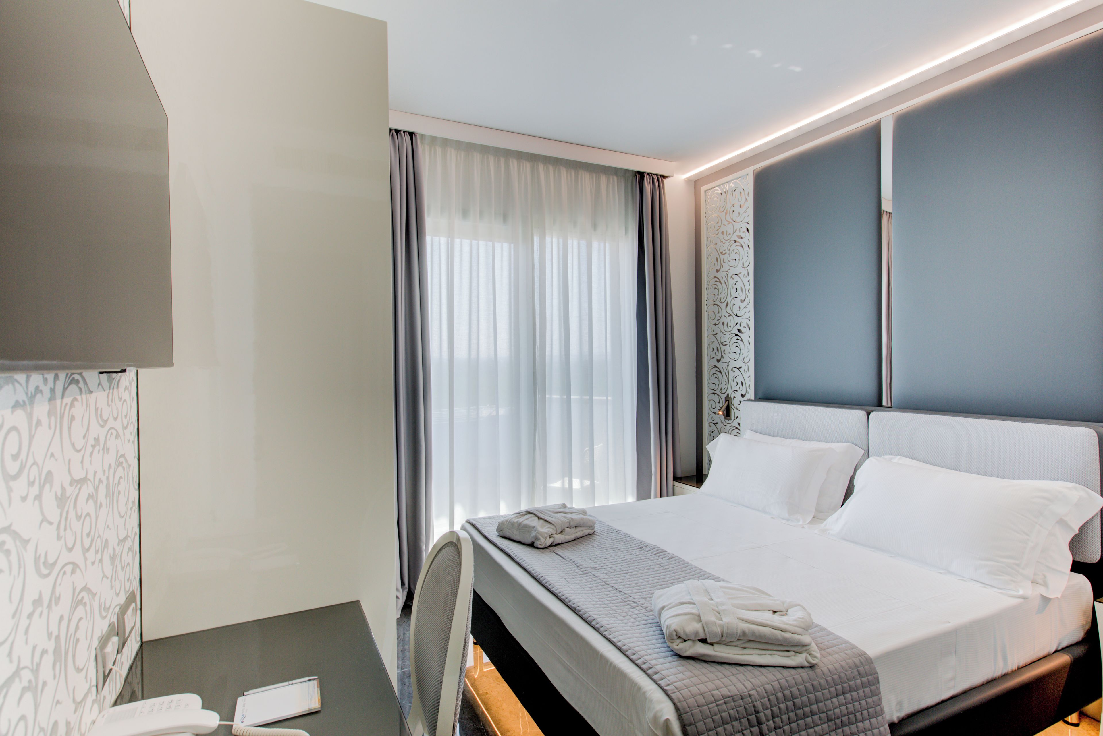 Una habitación de hotel con cama, escritorio, teléfono y ventana con cortinas.