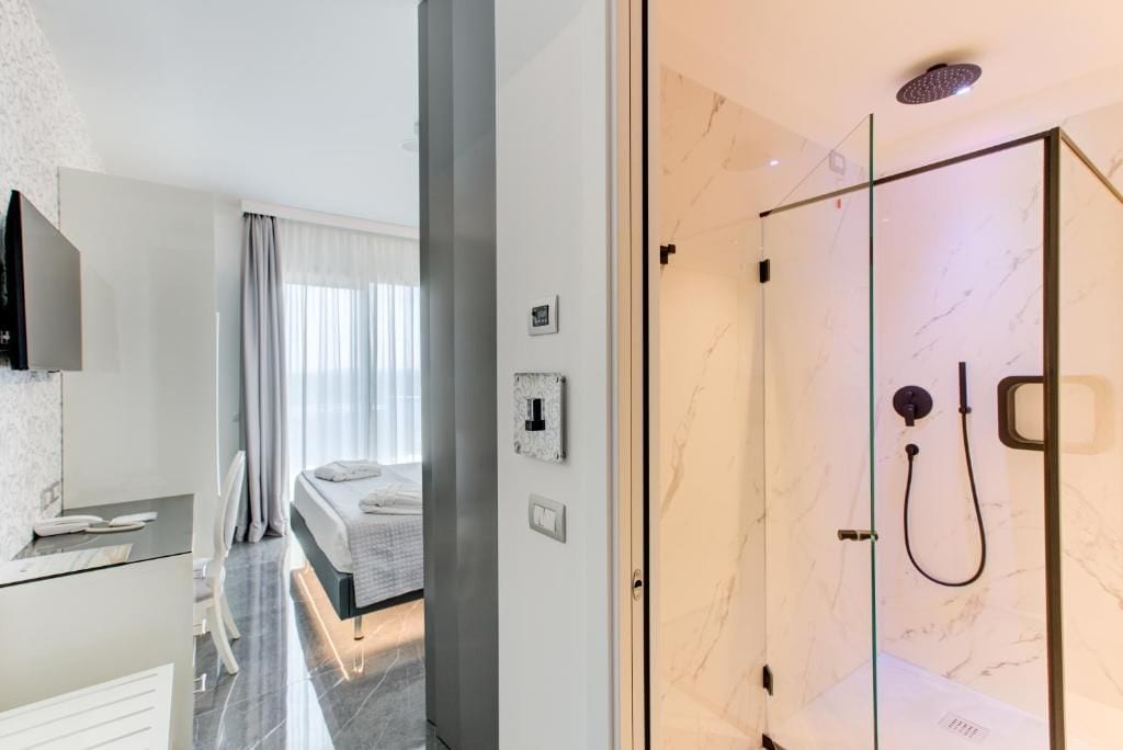Habitación de hotel moderna con ducha de vidrio, cama con vistas y escritorio con televisor de pantalla plana.