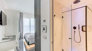 Habitación de hotel moderna con ducha de vidrio, cama con vistas y escritorio con televisor de pantalla plana.