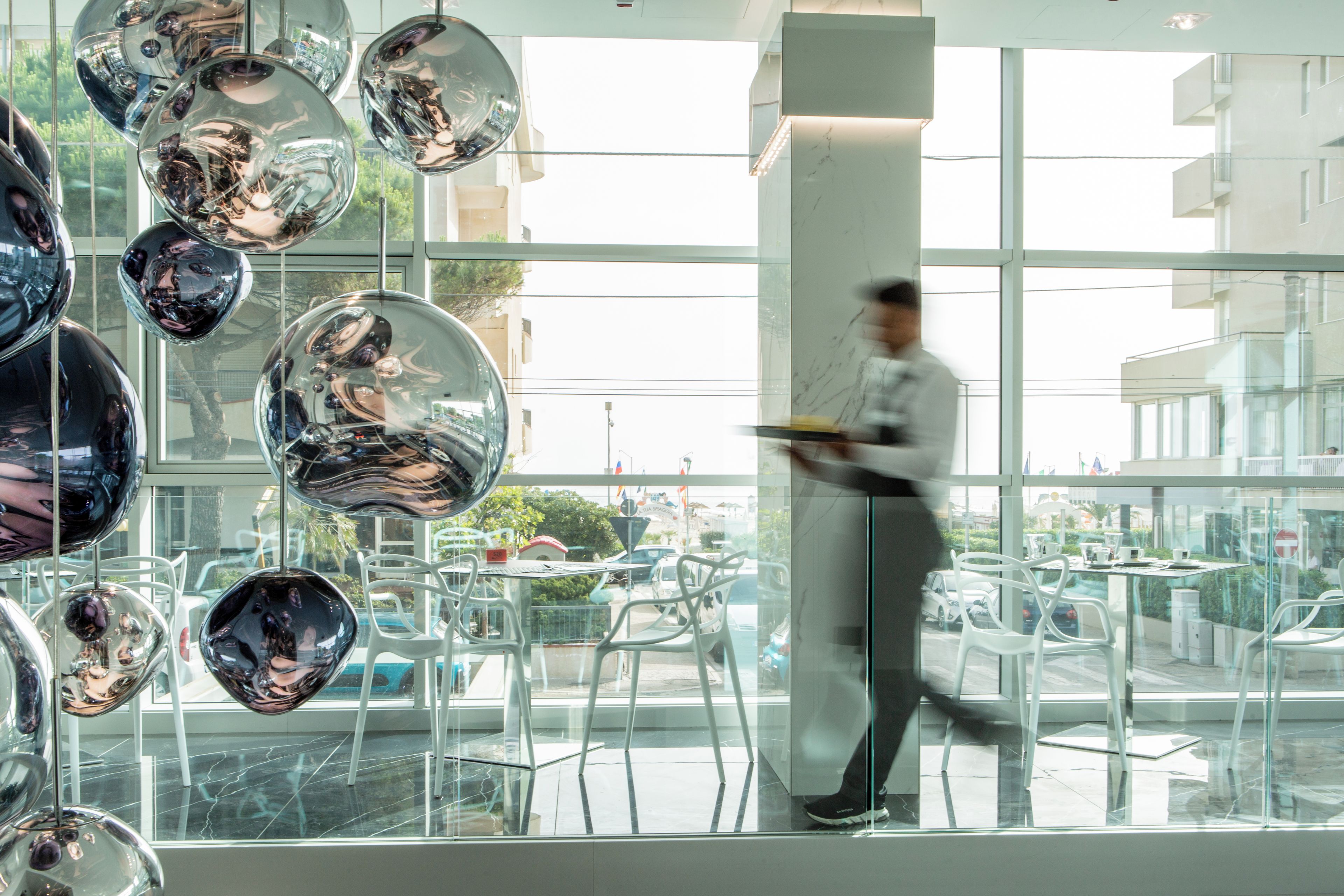 A modern interior with reflective spherical decorations, a person walking, and a view of the street outside.