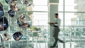 A modern interior with reflective spherical decorations, a person walking, and a view of the street outside.