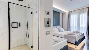 A modern hotel room with a glass-enclosed shower, a bed with a dark headboard, and a large window with curtains.