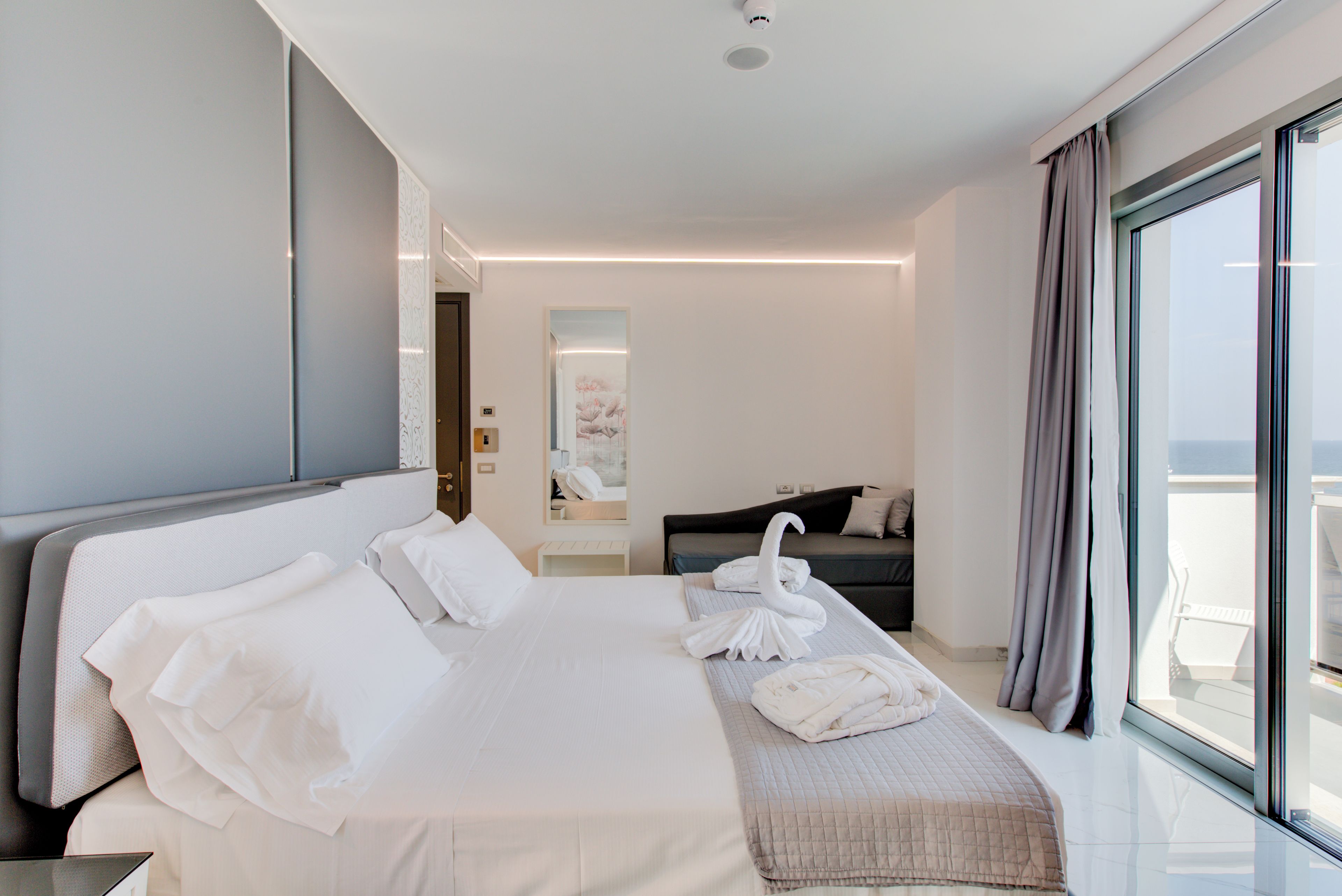 Quarto de hotel moderno com uma cama grande, um sofá, varanda com vista e um quadro na parede.