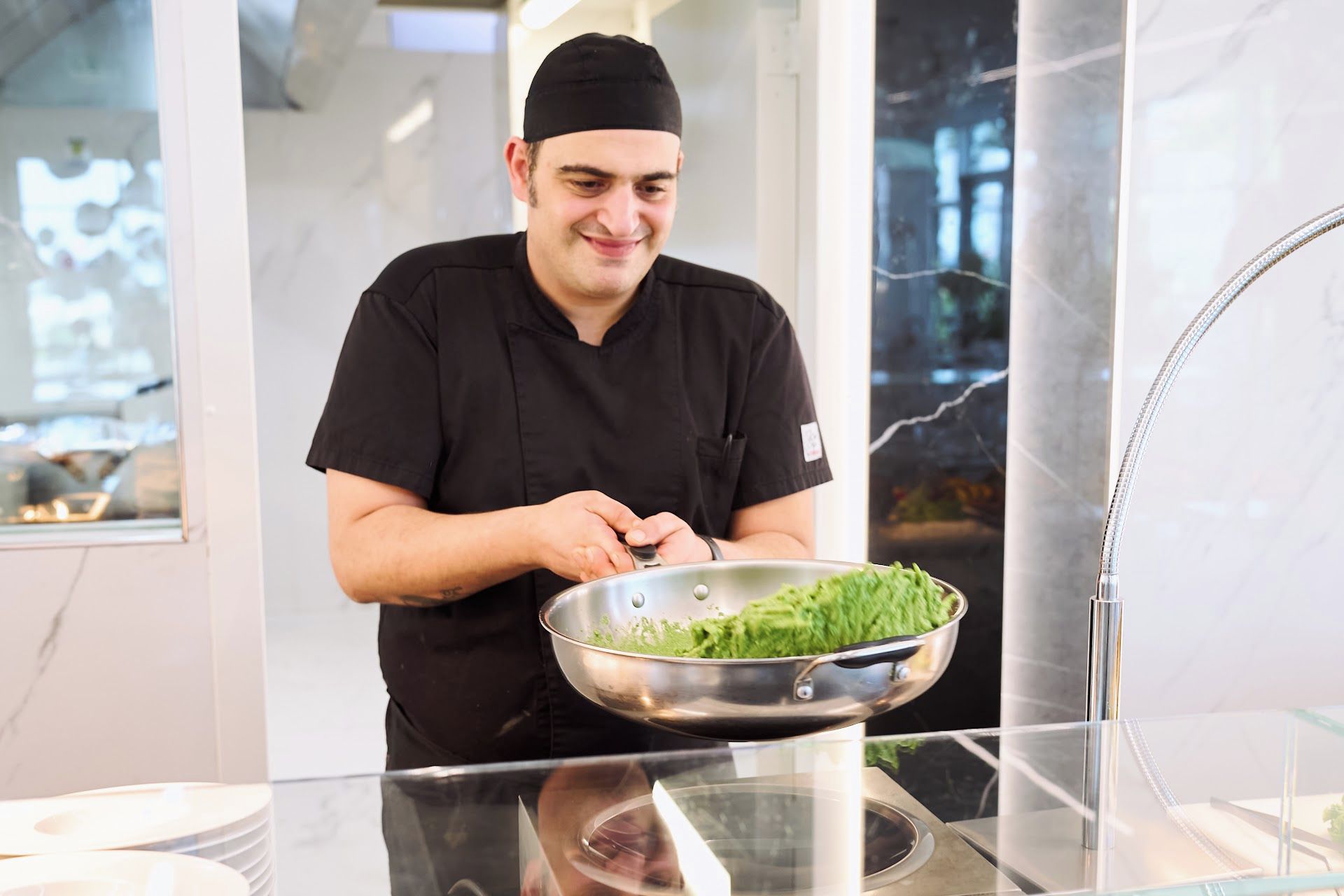 Una persona con uniforme negro preparando comida en un recipiente de acero inoxidable.