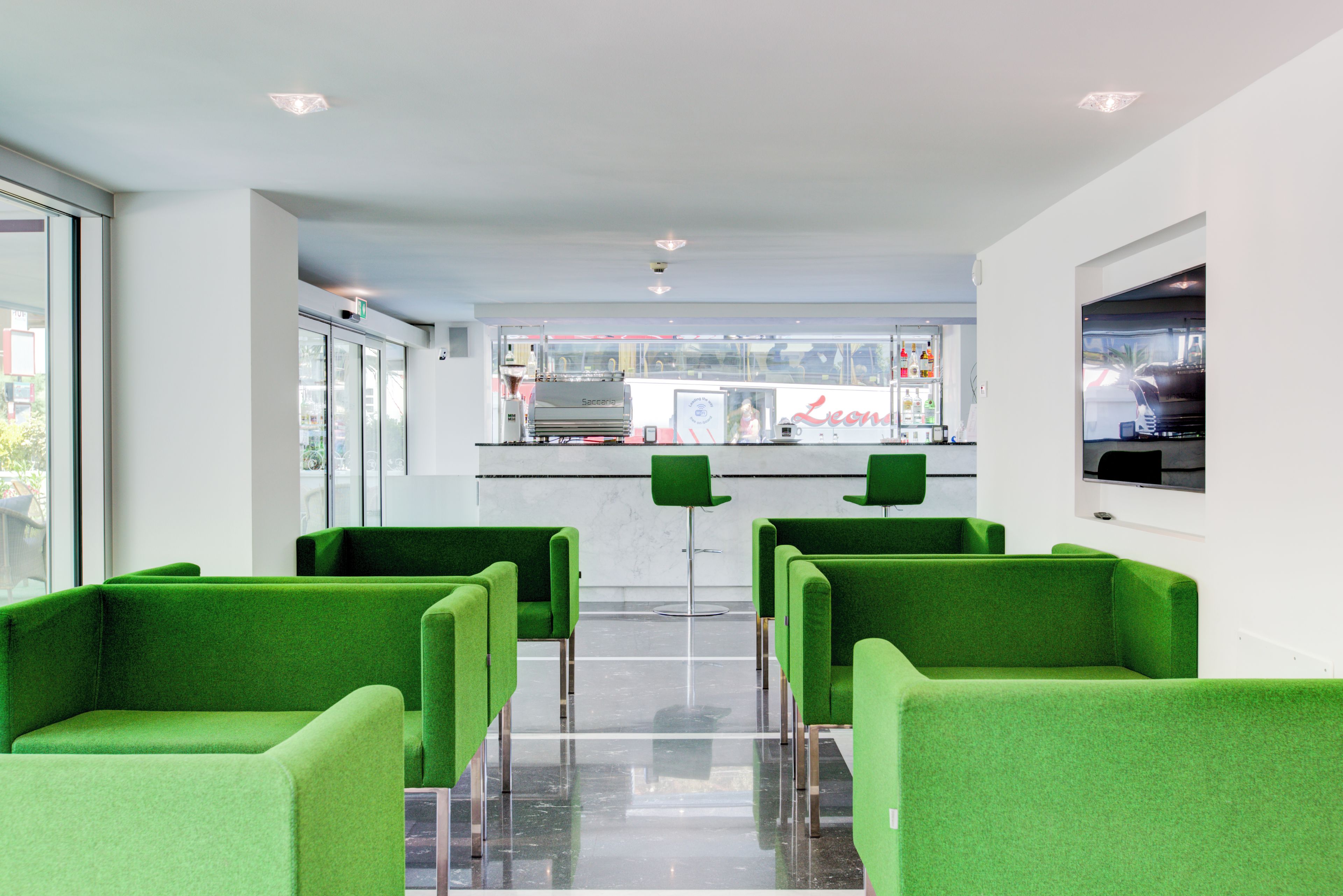 Un interior moderno con sillas verdes, una zona de bar y vistas a la calle.