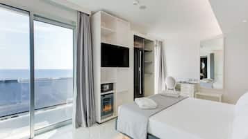 A modern hotel room with a large bed, a TV, a minibar, a walk-in closet, and a balcony with a city view.