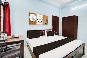 Habitación de hotel con cama, escritorio con tetera, armario y dos obras de arte en la pared.