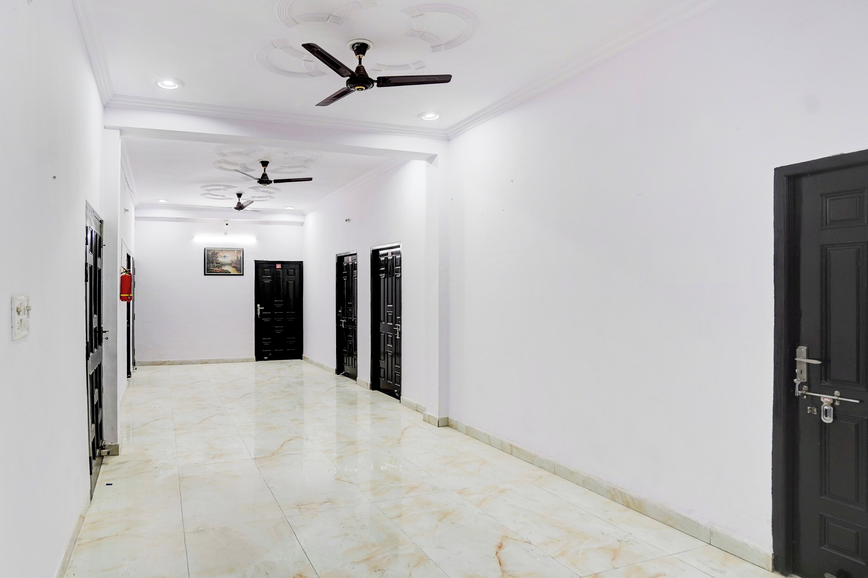 Un couloir avec un ventilateur de plafond, des portes noires et un extincteur.