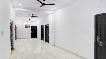 Un couloir avec un ventilateur de plafond, des portes noires et un extincteur.