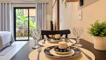 Mesa de comedor dispuesta con platos, cubiertos y vasos, con vista a un jardín por un ventanal corredero.