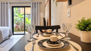 A dining table set with plates, cutlery, and glasses, with a view of a garden through a sliding door. - STUDIO 04 (Vinhedo)