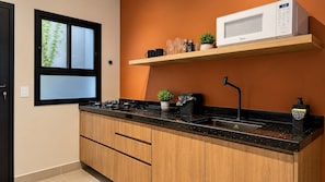A modern kitchen with a black countertop, wooden cabinets, a microwave, and a window with a view of greenery. - STUDIO 04 (Vinhedo)