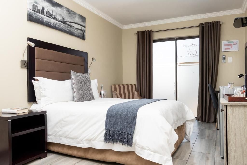 Habitación de hotel con una cama grande, una mesita de noche, un escritorio y vistas al exterior a través de una puerta de vidrio.