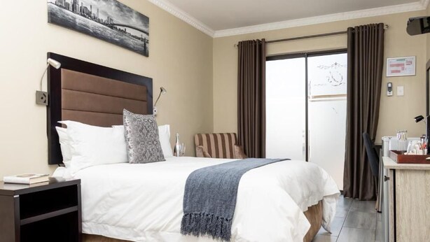 Een hotelkamer met een groot bed, een nachtkastje, een bureau en uitzicht buiten via een glazen deur.