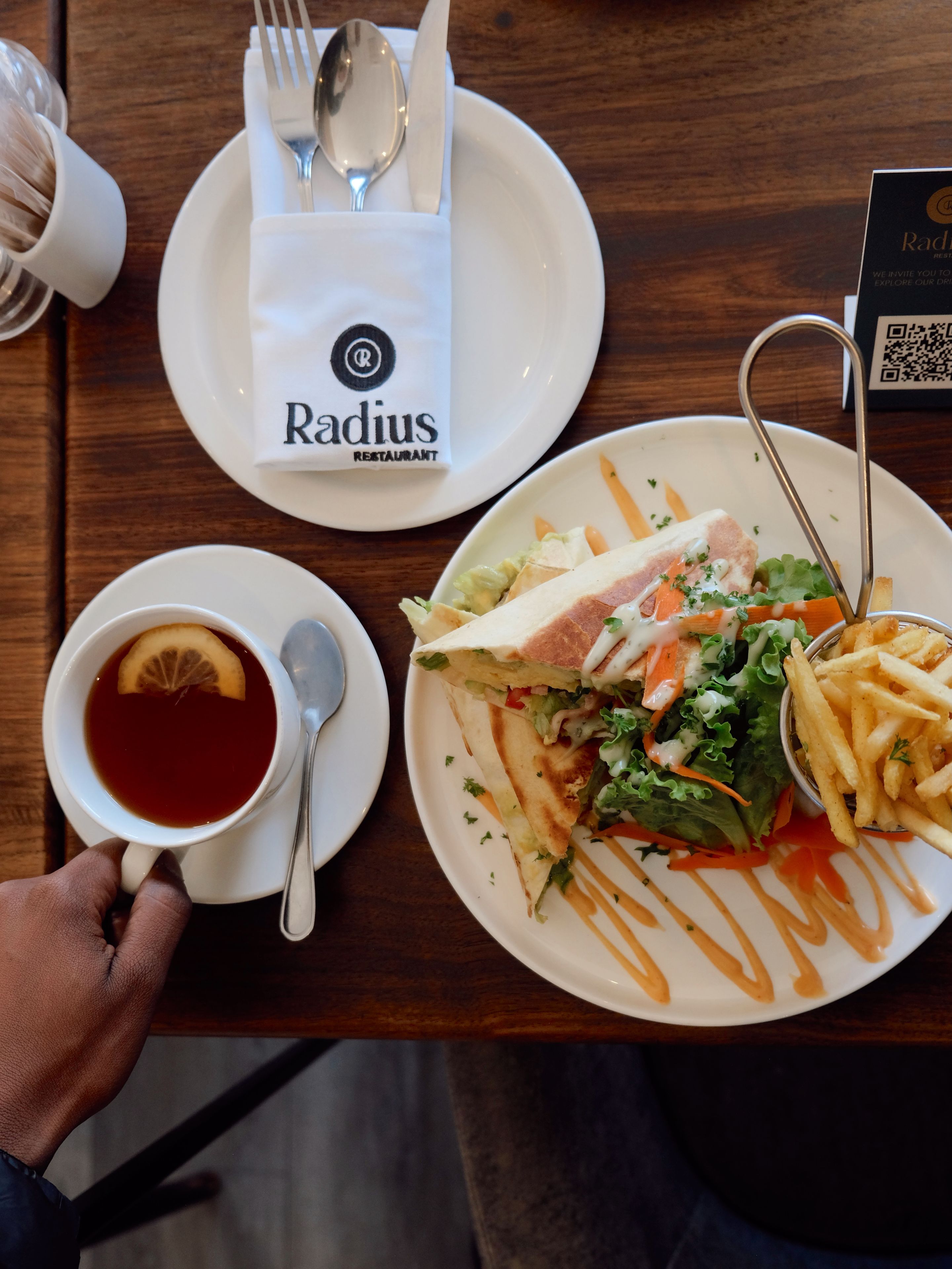 Uma refeição com sanduíche, batatas fritas e chá numa mesa de madeira.