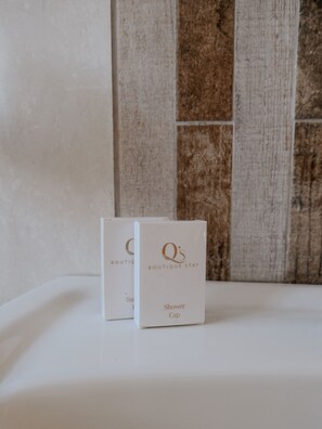 Two white boxes with 'Q's Boutique Stay' and 'Shower Cap' text on a white surface against a tiled wall. - Q's Boutique Stay (Standerton)