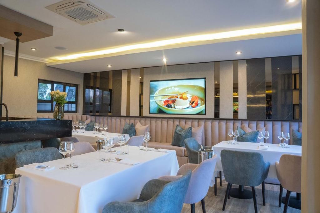 Un restaurante con varias mesas, asientos acolchados y una pantalla grande que muestra un plato.