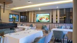 Een restaurant met meerdere eettafels, zachte zitplaatsen en een groot scherm waarop een gerecht wordt getoond.