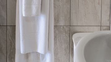A bathroom with a white bathtub, a towel rack with two towels, and a tiled floor.