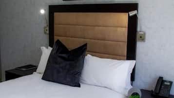 Une chambre d’hôtel avec un lit, une table de chevet avec un téléphone, un tableau encadré au mur et une petite plante sur la table de chevet.