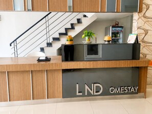 Un mostrador de recepción con una escalera al fondo, una planta y un refrigerador.