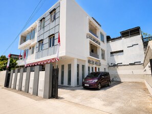 Un edificio de varios pisos con fachada blanca, balcones y un coche estacionado adelante.