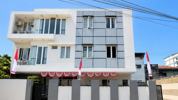 A modern two-story building with a gated entrance, air conditioning units on the balcony, and flags on poles. - Hotel O near Mall Panakkukang (Makassar)