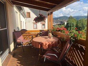 Eine Terrasse im Freien mit einem runden Tisch und Stühlen, einer Holzbank und einem hängenden Blumenkorb.