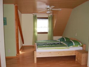 Ein Schlafzimmer mit schrägem Dach, einem Bett mit grüner Bettwäsche, einem hölzernen Nachttisch und einem Deckenventilator.