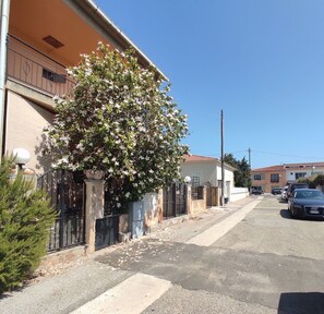 Eine Wohnstraße mit einem Haus, einem großen blühenden Baum, einem verschlossenen Eingang und einem parkenden Auto.