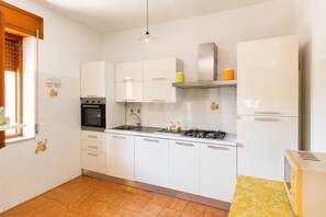 Eine Küche mit weißen Schränken, einem Herd, einem Backofen und einem Fenster mit Jalousien.
