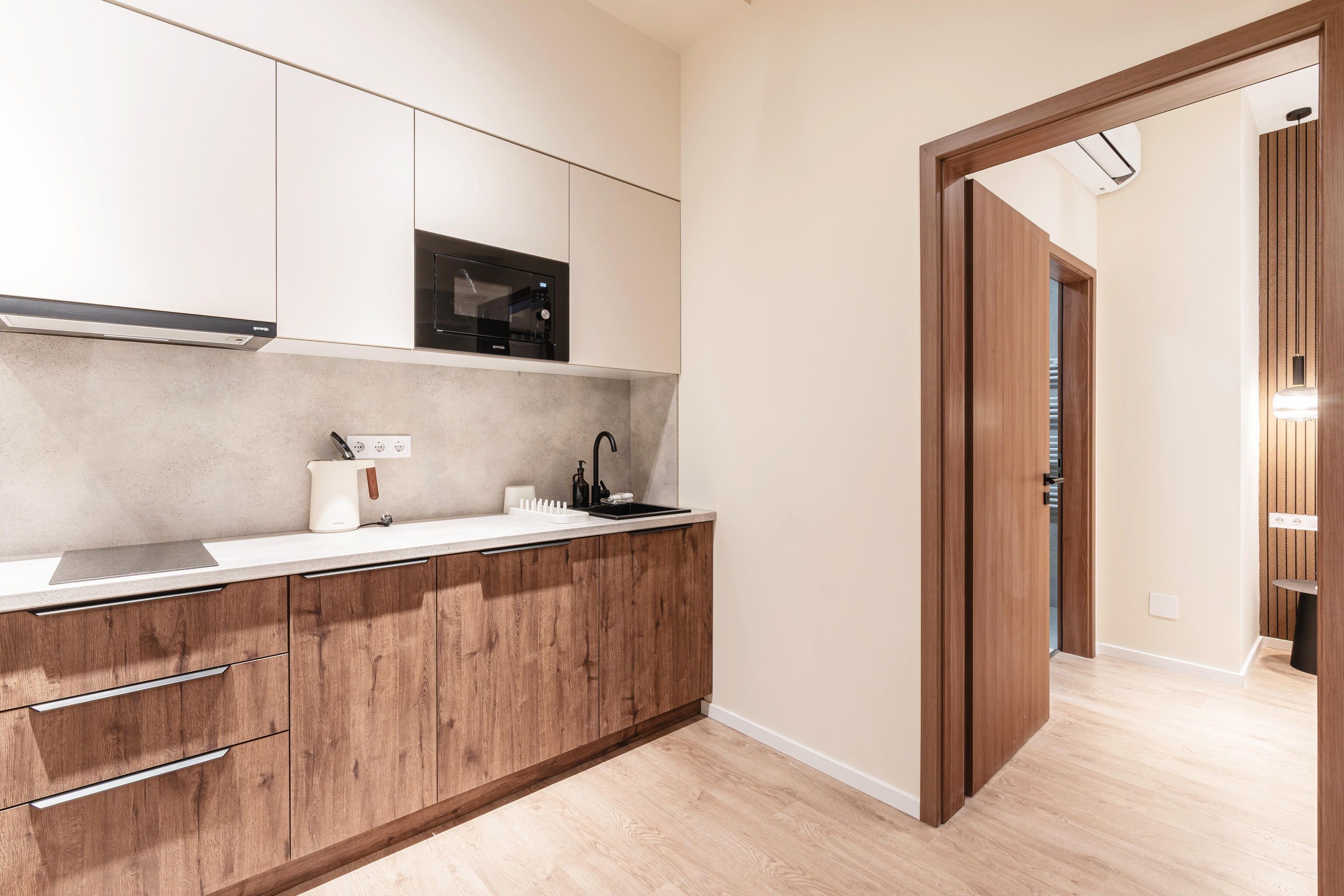 Cocina moderna con armarios de madera, microondas integrado y encimera con hervidor y dispensador de jabón.