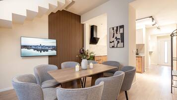 Un comedor moderno con una mesa de madera, sillas tapizadas en gris, un televisor de pantalla plana y un cuadro de un paisaje urbano.