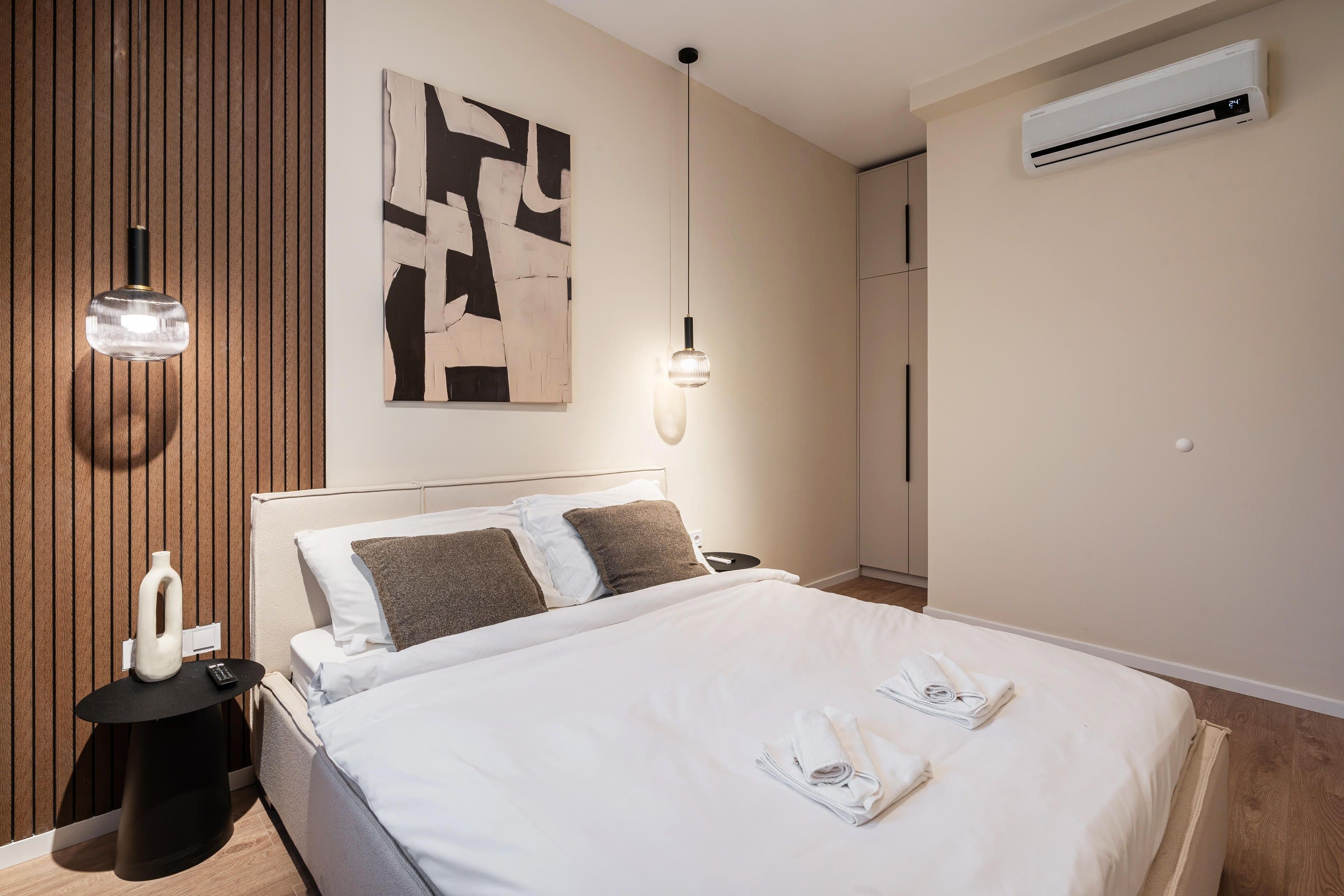 Une chambre d’hôtel moderne avec un grand lit, un climatiseur fixé au mur et un tableau abstrait contemporain.