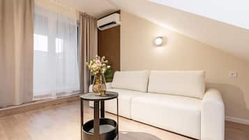Una sala de estar moderna con un sofá blanco, una mesita redonda con un florero y un equipo de aire acondicionado en la pared.