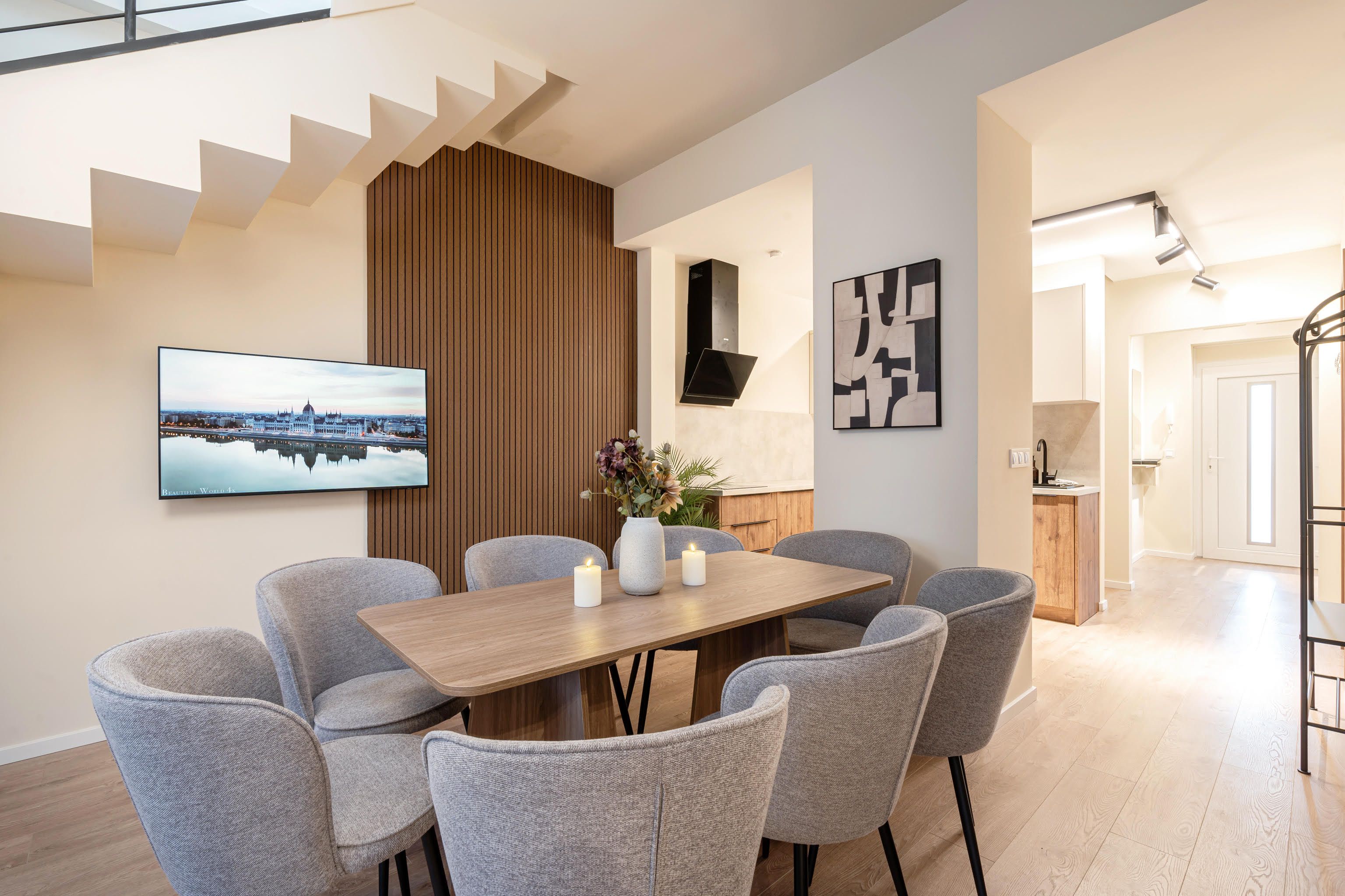 Een moderne eetruimte met een houten tafel, grijs gestoffeerde stoelen, een flatscreen televisie en een stadslandschap schilderij.