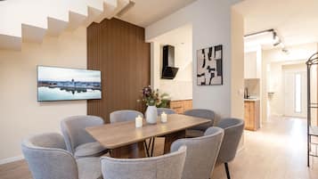 Een moderne eetruimte met een houten tafel, grijs gestoffeerde stoelen, een flatscreen televisie en een stadslandschap schilderij.