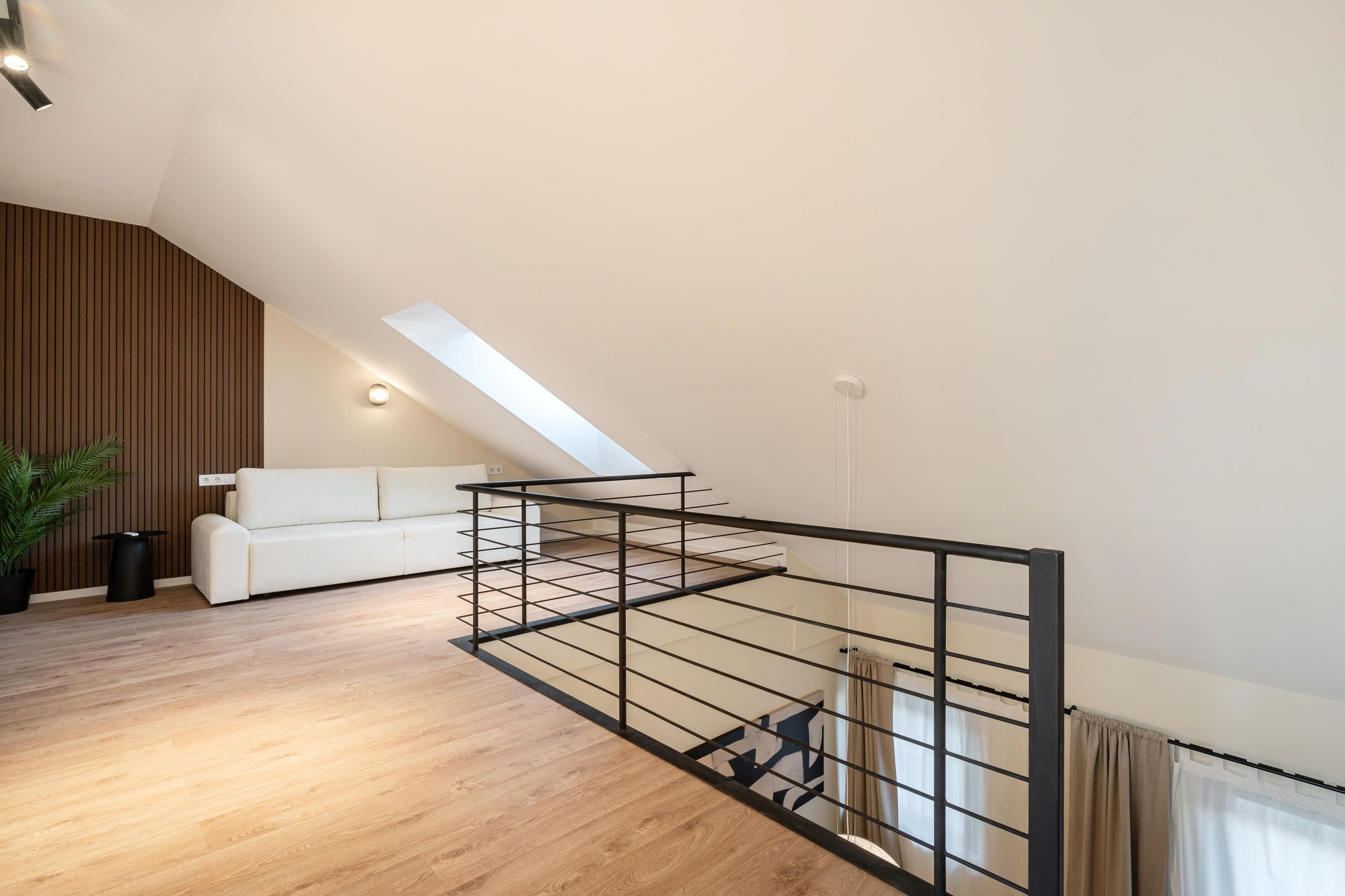 Un dormitorio tipo loft moderno con techo inclinado, un sofá blanco, piso de madera y baranda de metal.