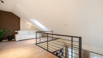 Un dormitorio tipo loft moderno con techo inclinado, un sofá blanco, piso de madera y baranda de metal.