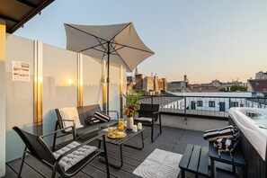 Una terrassa a la teulada amb zona de seients, banyera hidromassatge i vista a la ciutat.