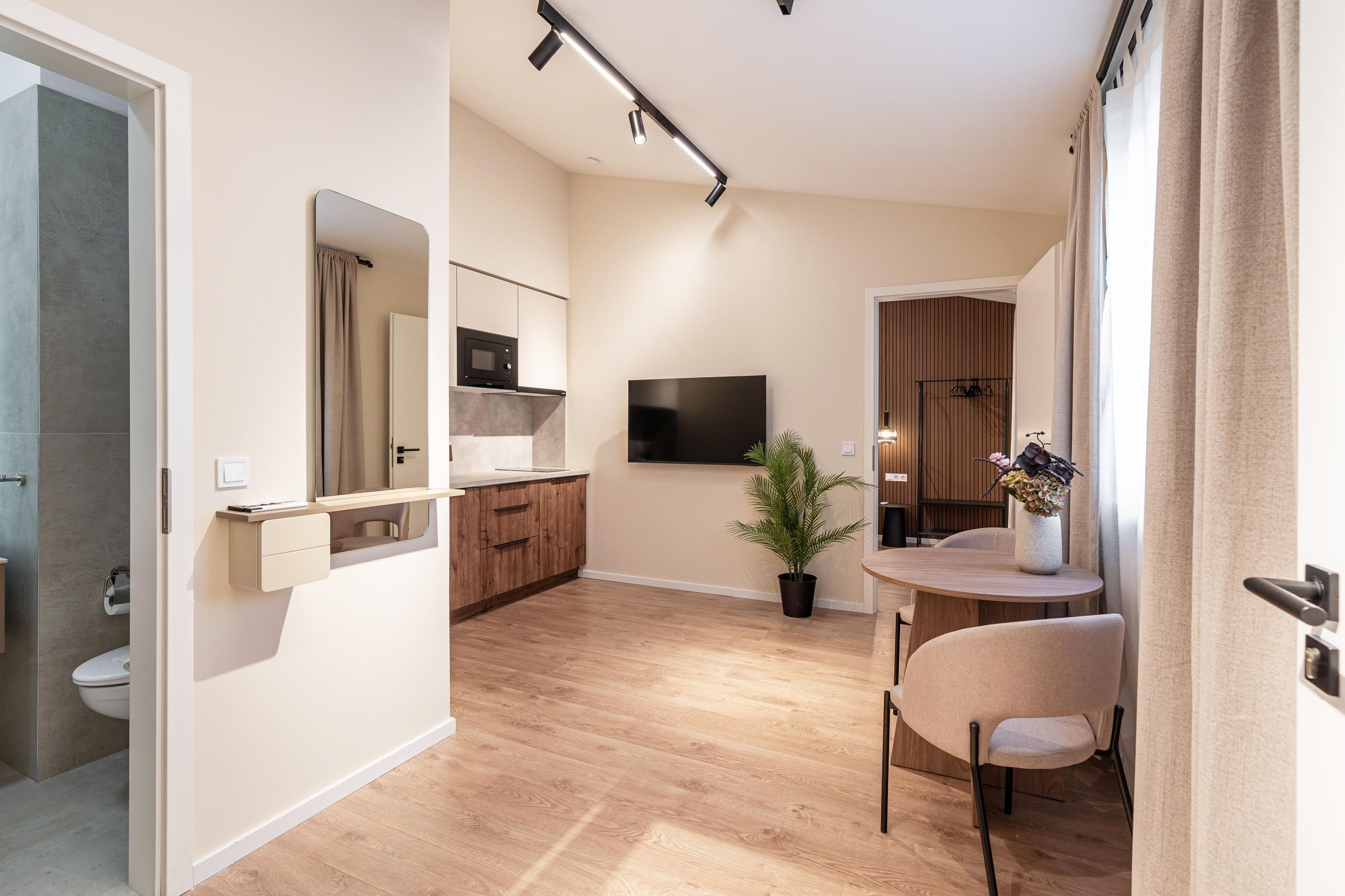 Un salon moderne doté d’un téléviseur à écran plat, d’une table à manger avec des chaises, d’une petite plante en pot et d’un coin cuisine avec un four à micro-ondes.
