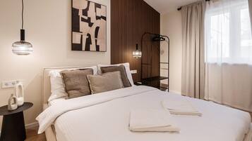 Una cama bien hecha con sábanas blancas y dos toallas, un cuadro abstracto moderno en la pared, una lámpara de pie y un panel de pared de madera.