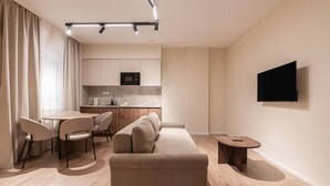 A modern living room with a sofa, chairs, a dining table, and a kitchen area in the background. - LimeTree Residence by BQA (Budapest)