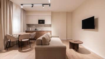 Een moderne woonkamer met een bank, een eettafel, stoelen, een keukenhoek en een flatscreen televisie aan de muur.